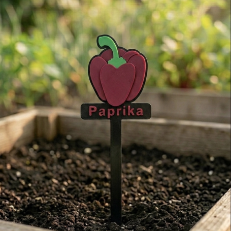 Rote Paprika-Pflanze mit Etikett in einem Gartenbeet.