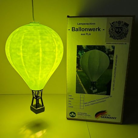 Leuchtende Luftballonlampe in grün neben einer Verpackung.