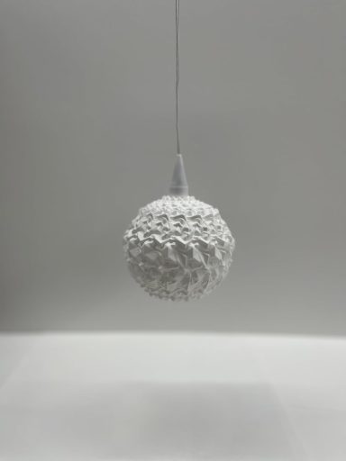 Weiße, strukturierte Kugel hängt an einer Schnur vor grauem Hintergrund.