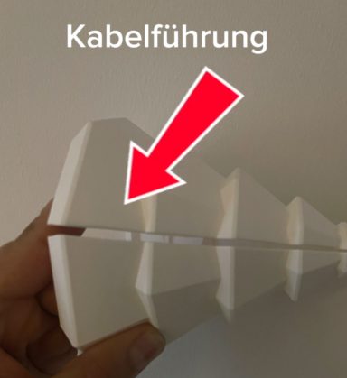 Weißes Kabelführungselement mit hervorgehobener Trennstelle in der Hand gehalten.