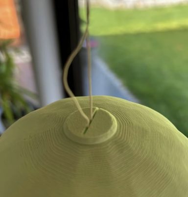 Grüner Keramiktopf mit Faden zum Aufhängen, im Hintergrund grünes Gras.