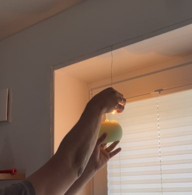 Eine Hand hält eine grüne Kugel vor einem Fenster mit Rollläden.