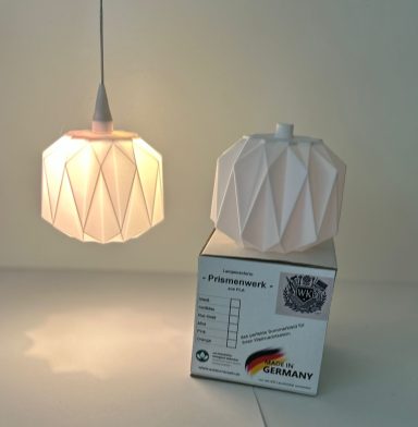 Hängelampe in geometrischer Form, Leuchtmittel leuchtet warm, weißer Karton darunter.