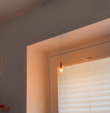 Hängende Glühbirne über einem Fenster mit Jalousien.