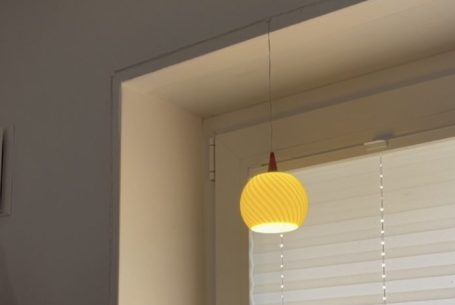 Gelbe Pendelleuchte hängt über einem Fenster mit Rollläden.