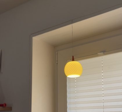 Gelbe Hängeleuchte hängt an einer Wand, vor einem Fenster mit Jalousien.