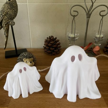 Zwei weiße Geisterlaternen mit braunen Augen auf einem Tisch, umgeben von Deko.